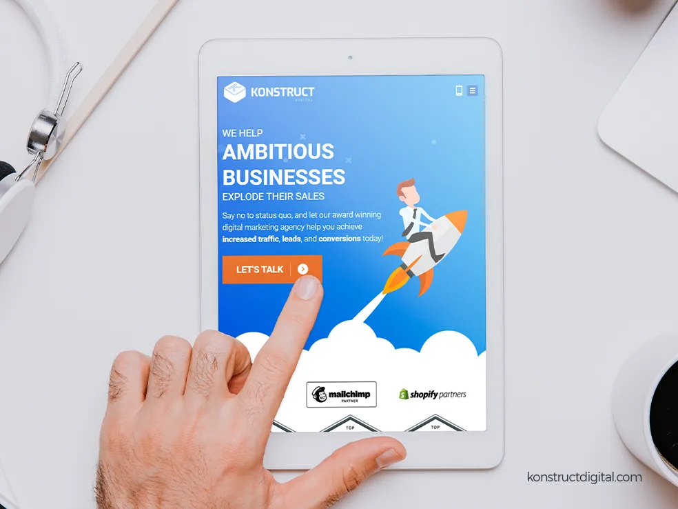 A tablet with the Konstruct homepage on the screen and a hand tapping
the screen