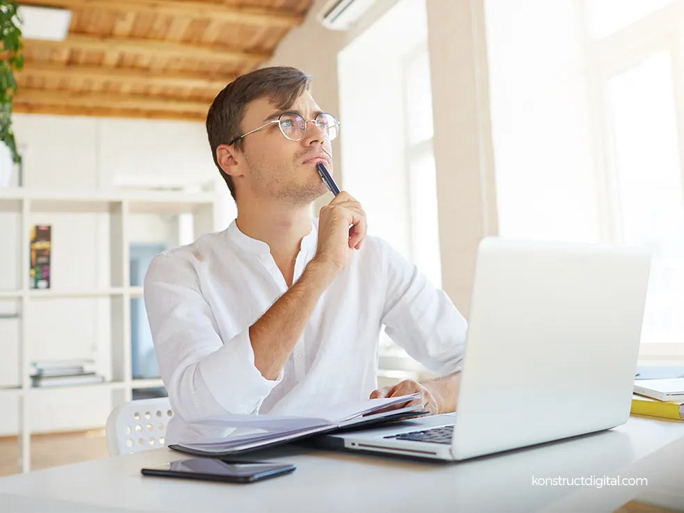 Mans sitting at his desk with a pen in his mouth thinking about something. 