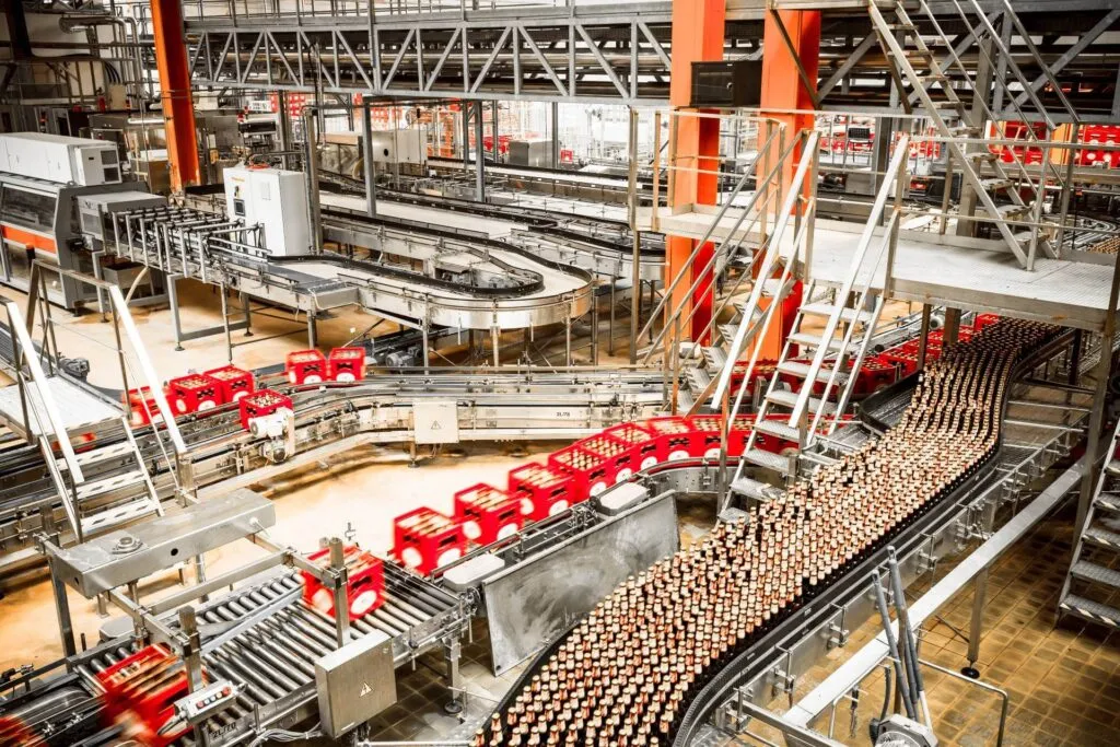 Automated beverage production and packaging line inside a large-scale food manufacturing facility with red plastic crates and conveyor belts