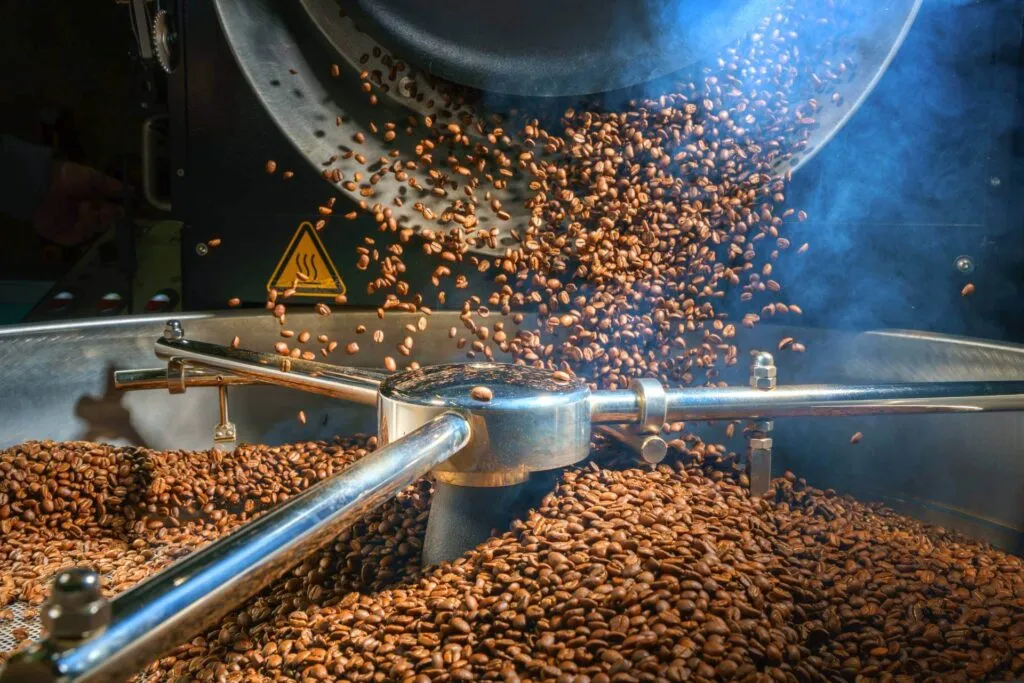 Roasted coffee beans pouring into industrial cooling tray inside food processing facility