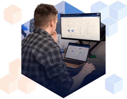A person reviews SEO performance dashboards on a widescreen monitor and laptop, showing traffic charts, keyword data, and a geographic reach map.