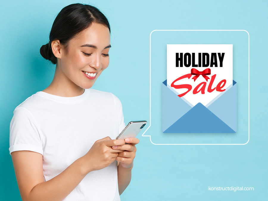 A woman looking at her phone with a "holiday sale" email popping out of the screen