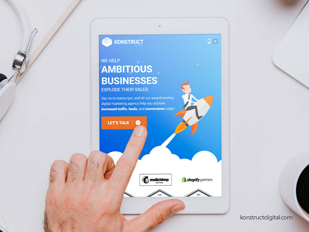 A tablet with the Konstruct homepage on the screen and a hand tapping
the screen