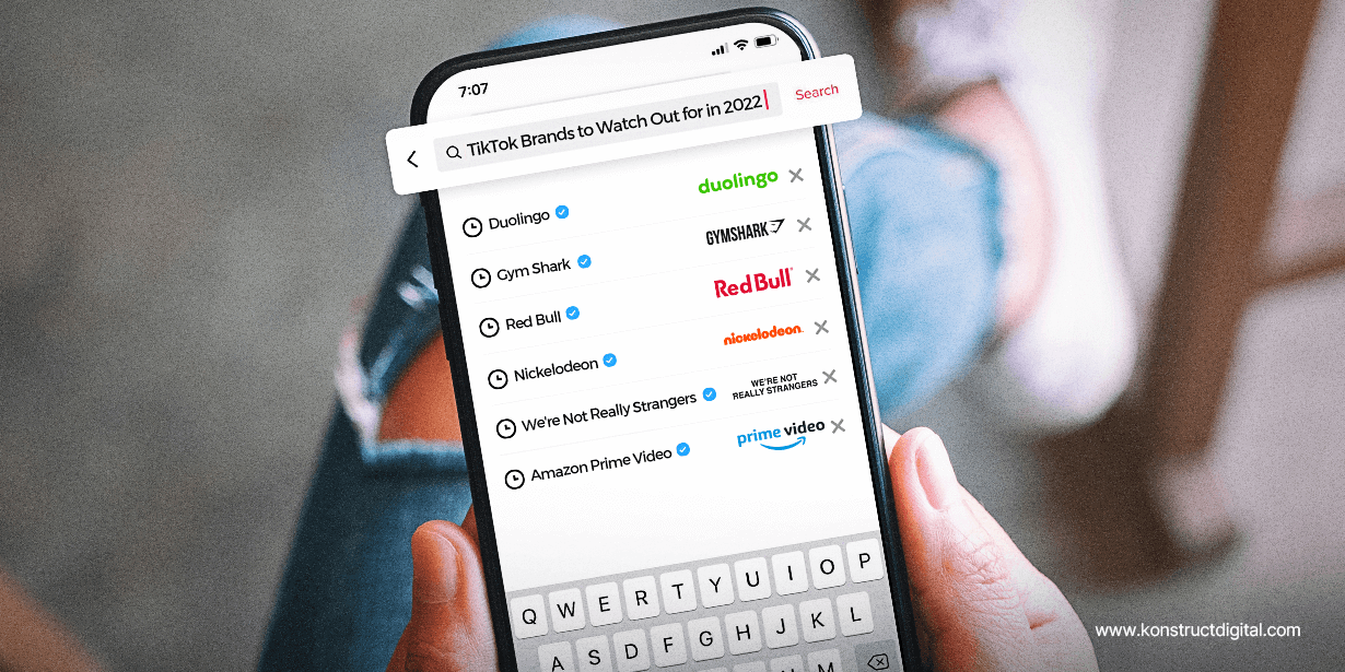 A phone with the TikTok search bar on the screen. The search is "TikTok Brands to Watch Our for in 2022" with Duolingo, Gym Shark, Red Bull, Nickelodeon, We're Not Really Strangers, and Amazon Prime Video featured.