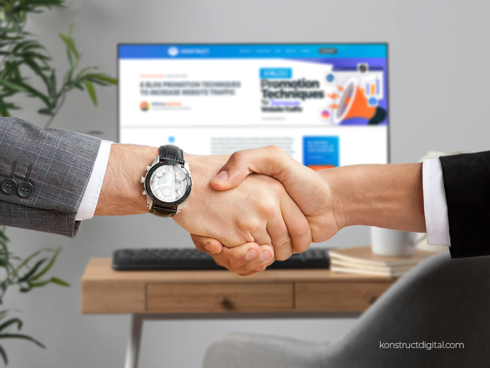 Two people shaking hands in front of a computer with Konstructs blog, 8 Blog Promotion Techniques to Increase Website Traffic, on the screen.