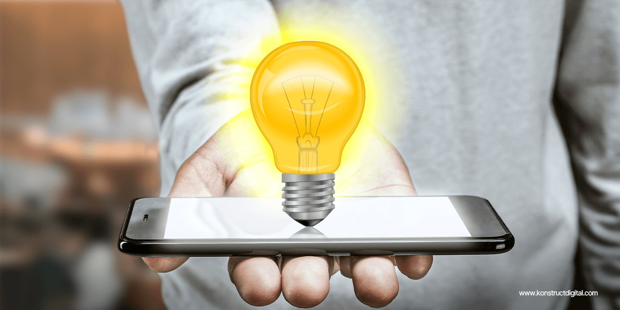 A person holding their phone with an illuminated light bulb hovering above.