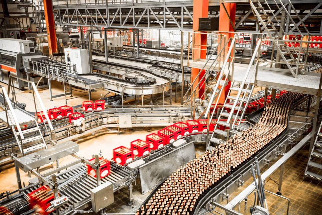 Automated beverage production and packaging line inside a large-scale food manufacturing facility with red plastic crates and conveyor belts